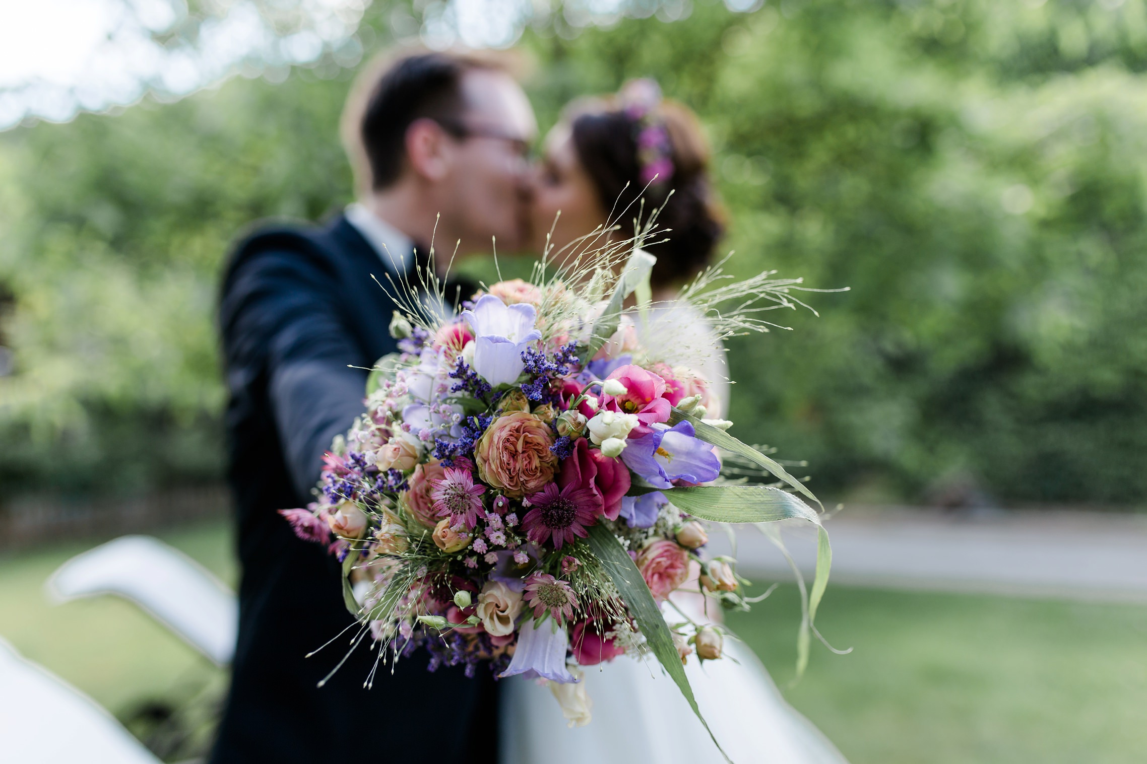 Das Hochzeitspaar küsst sich hinter dem Brautstrauß - bei diesem Foto ist nur der Brautstrauss im Fokus