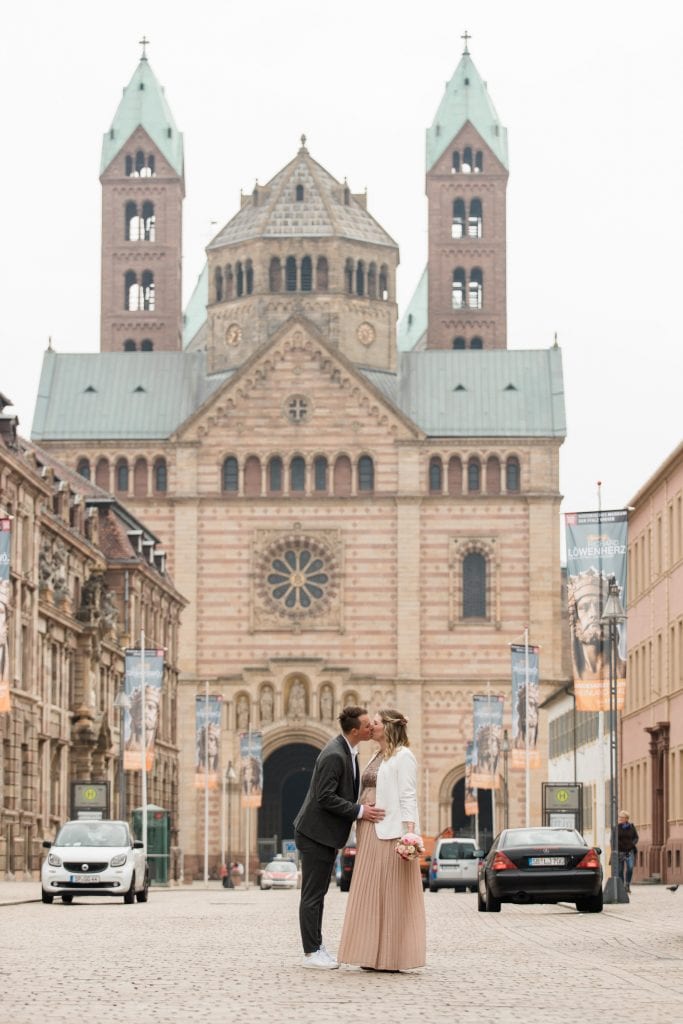 Ein verliebtes Hochzeitspaar steht auf der Maximilianstraße und küsst sich. Im Hintergrund ist der Dom zu Speyer zu sehen.