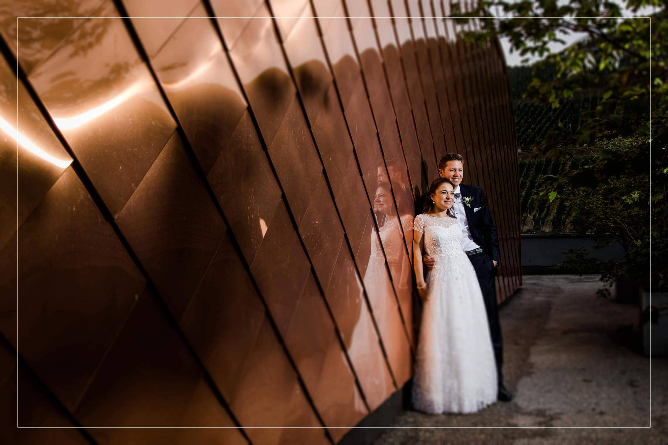 Titelbild zum Blogbeitrag über eine wunderschöne Hochzeit im Gut Hermannsberg - das Brautpaar posiert vor einer Kupferwand.