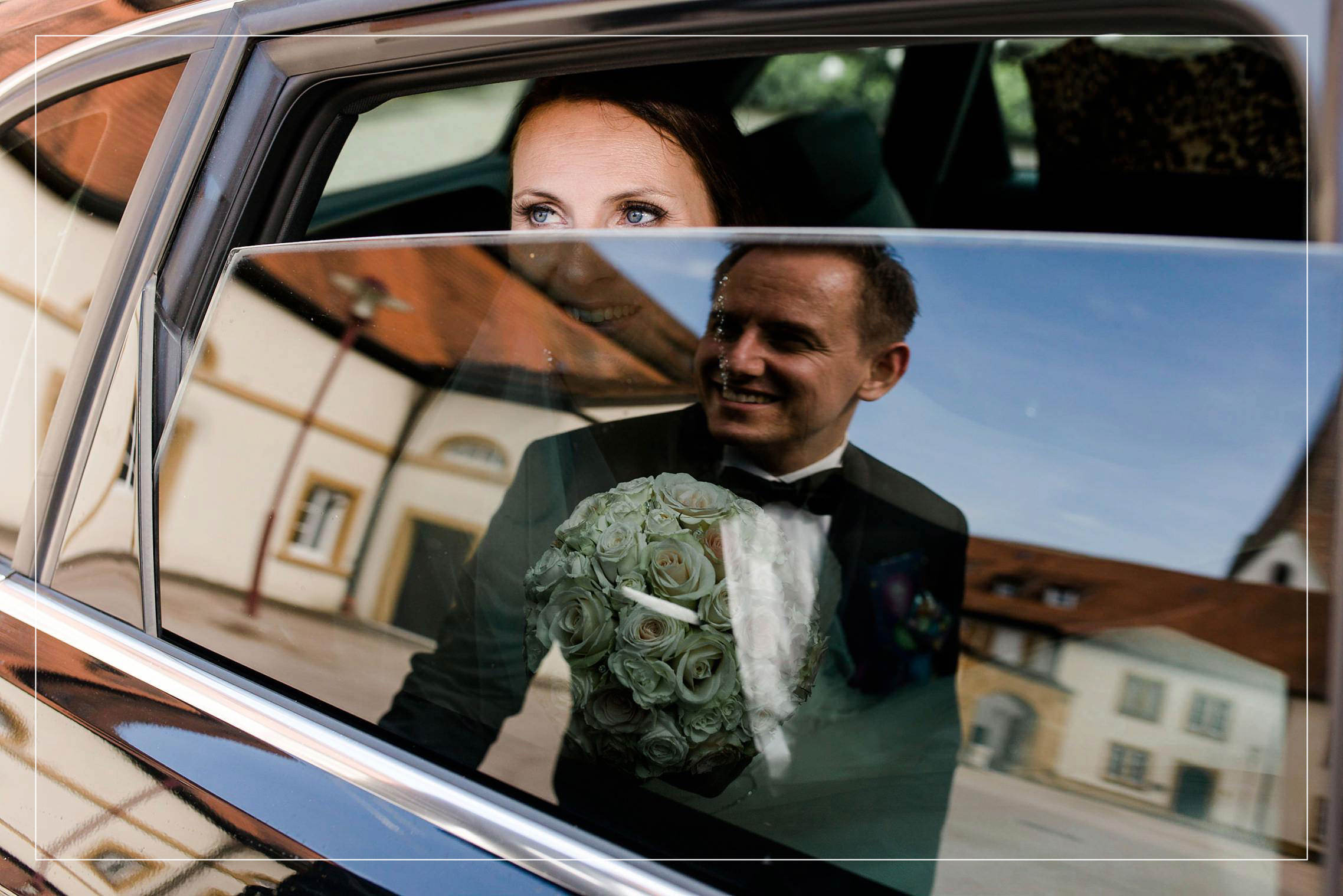 Bräutigam spiegelt sich im Autofenster, Braut schaut ihn verliebt an.