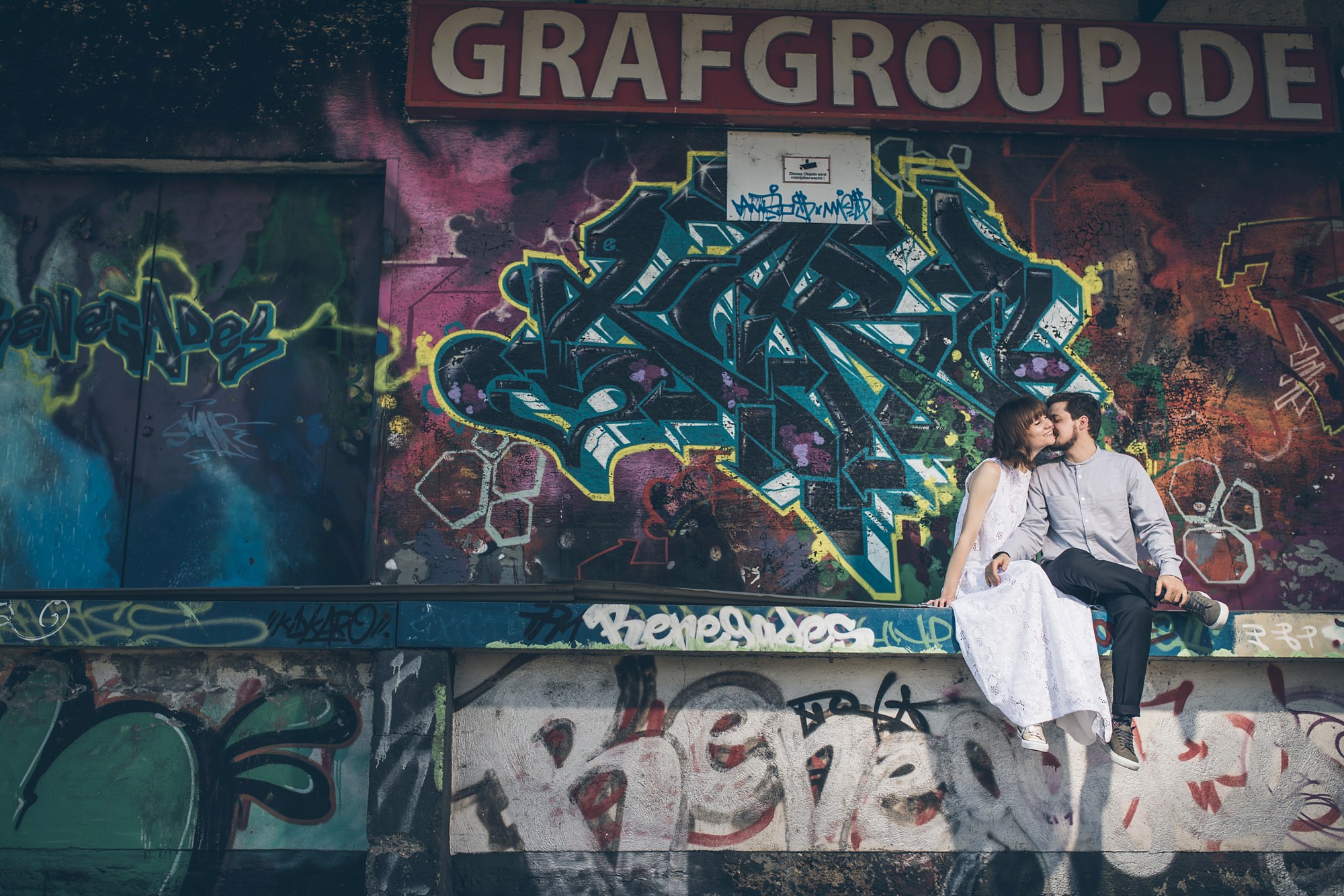 Braut und Bräutigam flirten vor großem Graffiti auf Laderampe im Jungbusch Mannheim.