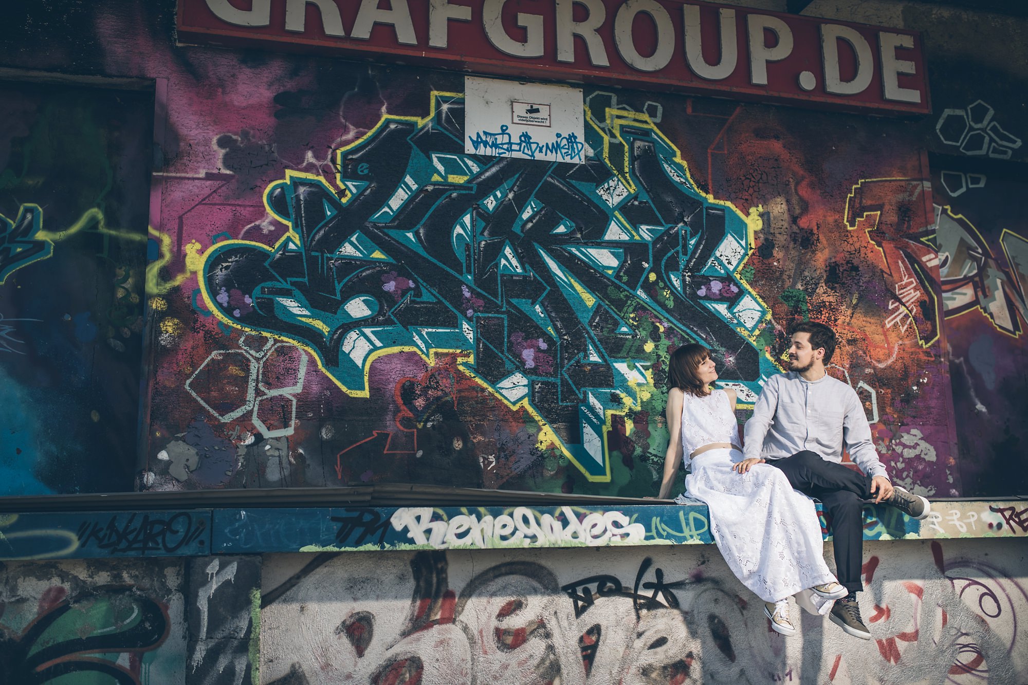 Braut und Bräutigam flirten vor großem Graffiti auf Laderampe im Jungbusch Mannheim.
