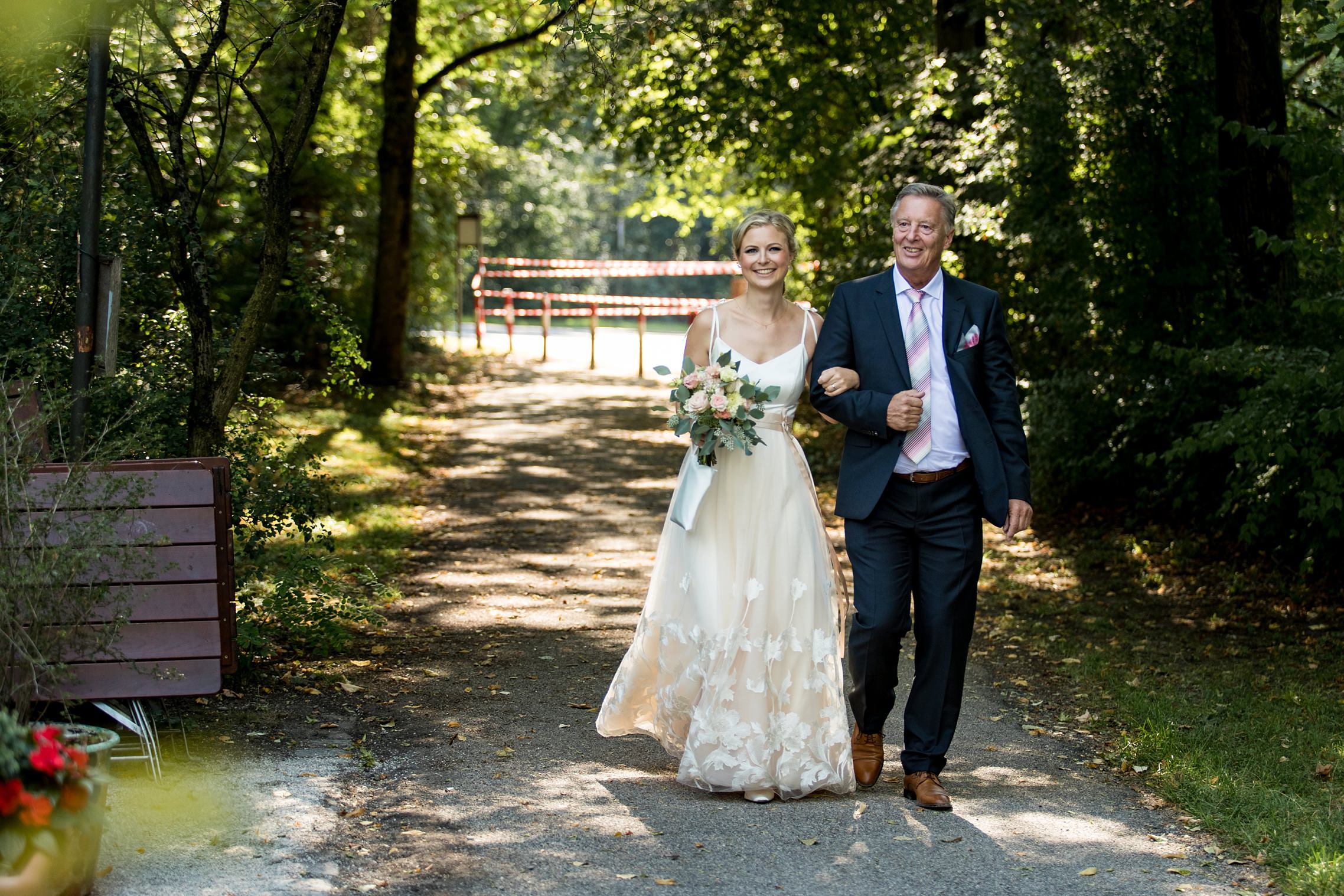 Braut wird von ihrem Vater zur Trauung gebracht, Hochzeit im Englischen Garten in München